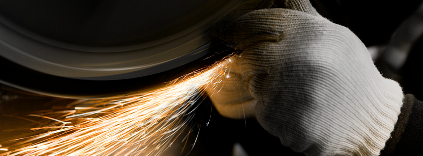Close-up of a gloved hand grinding metal, producing sparks in a workshop setting.
