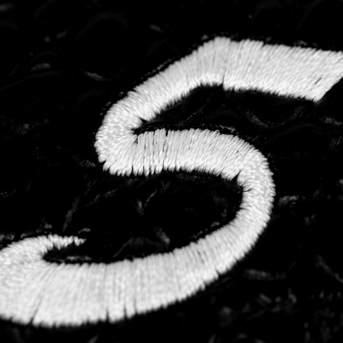 Close-up of an embroidered number 5 in white thread on a black background.
