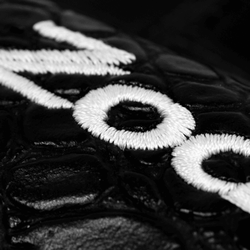 Close-up of iron cover with detailed white embroidery on black leather-like material.